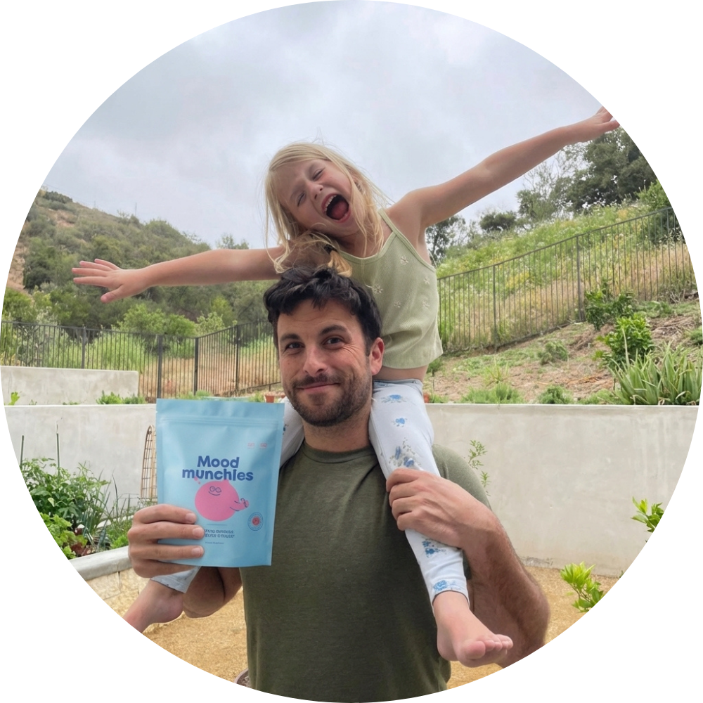 A man holds a bag of Mood Munchies while a young girl sits happily on his shoulders.