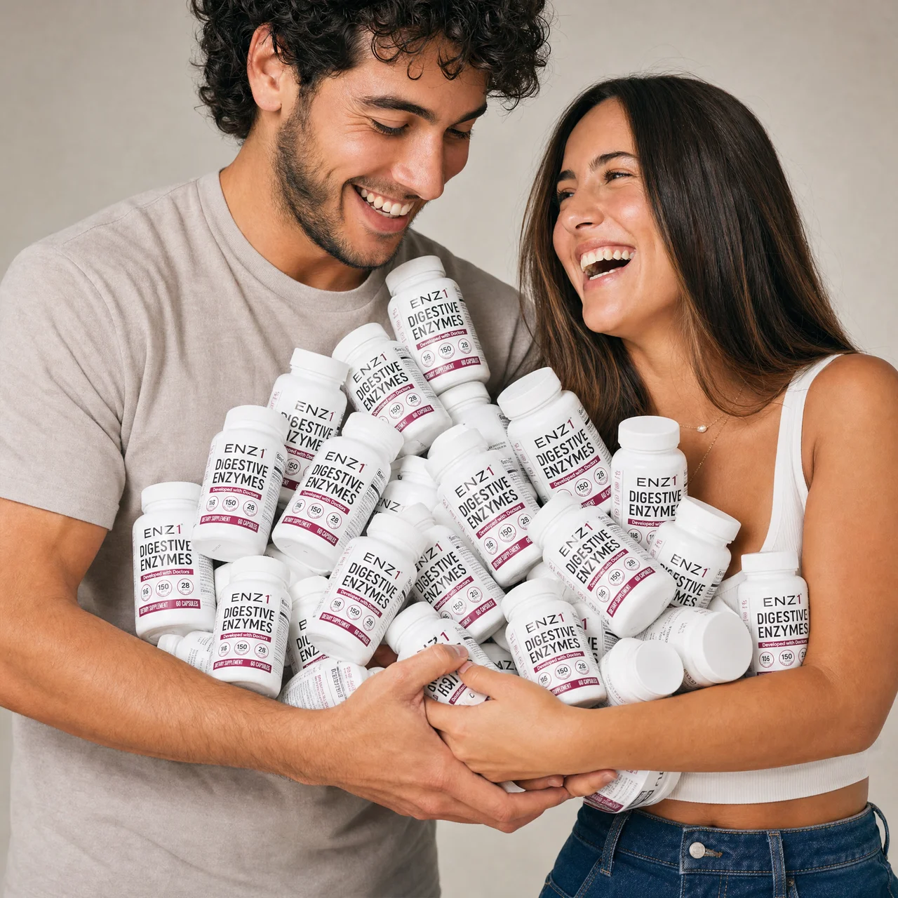 A smiling couple holds a large pile of ENZ1 Digestive Enzymes supplement bottles.