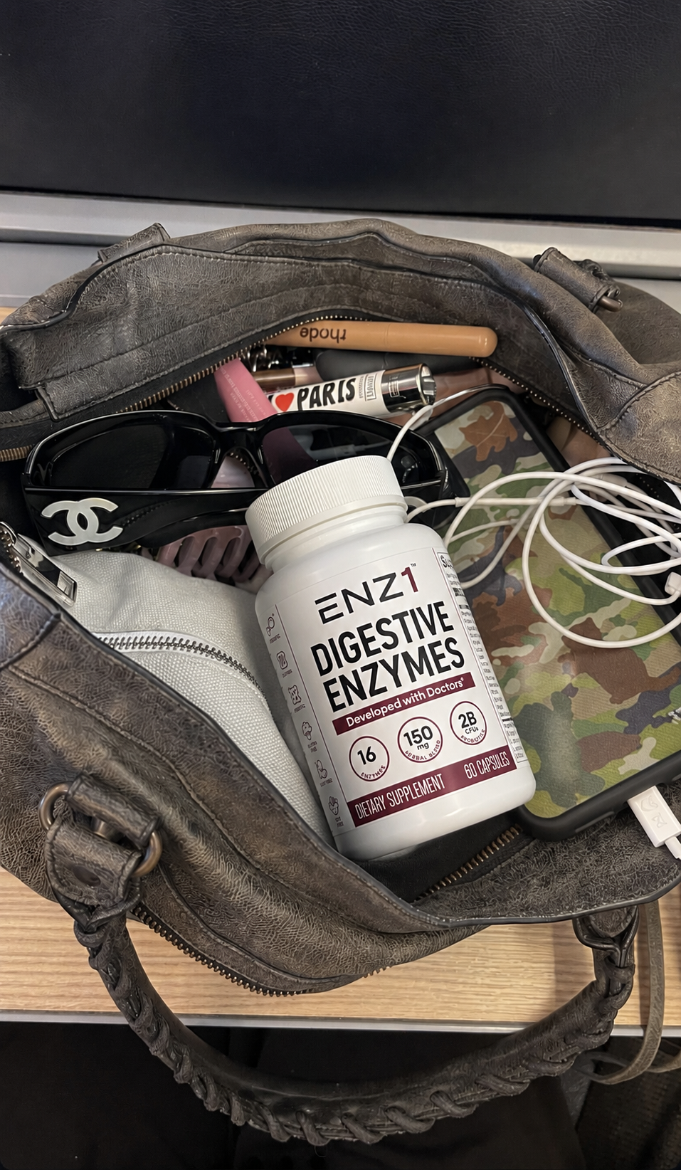 An open, distressed gray leather handbag showing its contents, including a bottle of digestive enzymes and sunglasses.