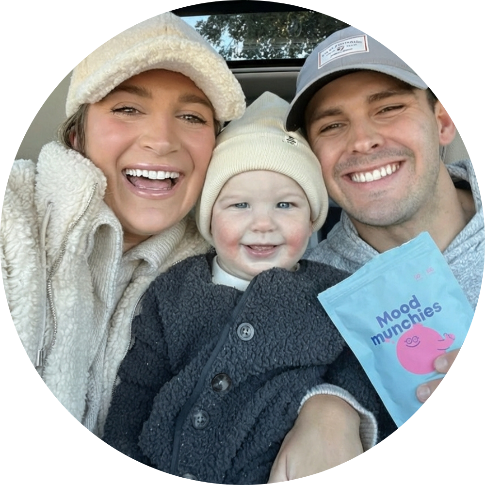 A smiling family of three takes a selfie in a car, holding a blue pouch of Mood Munchies.