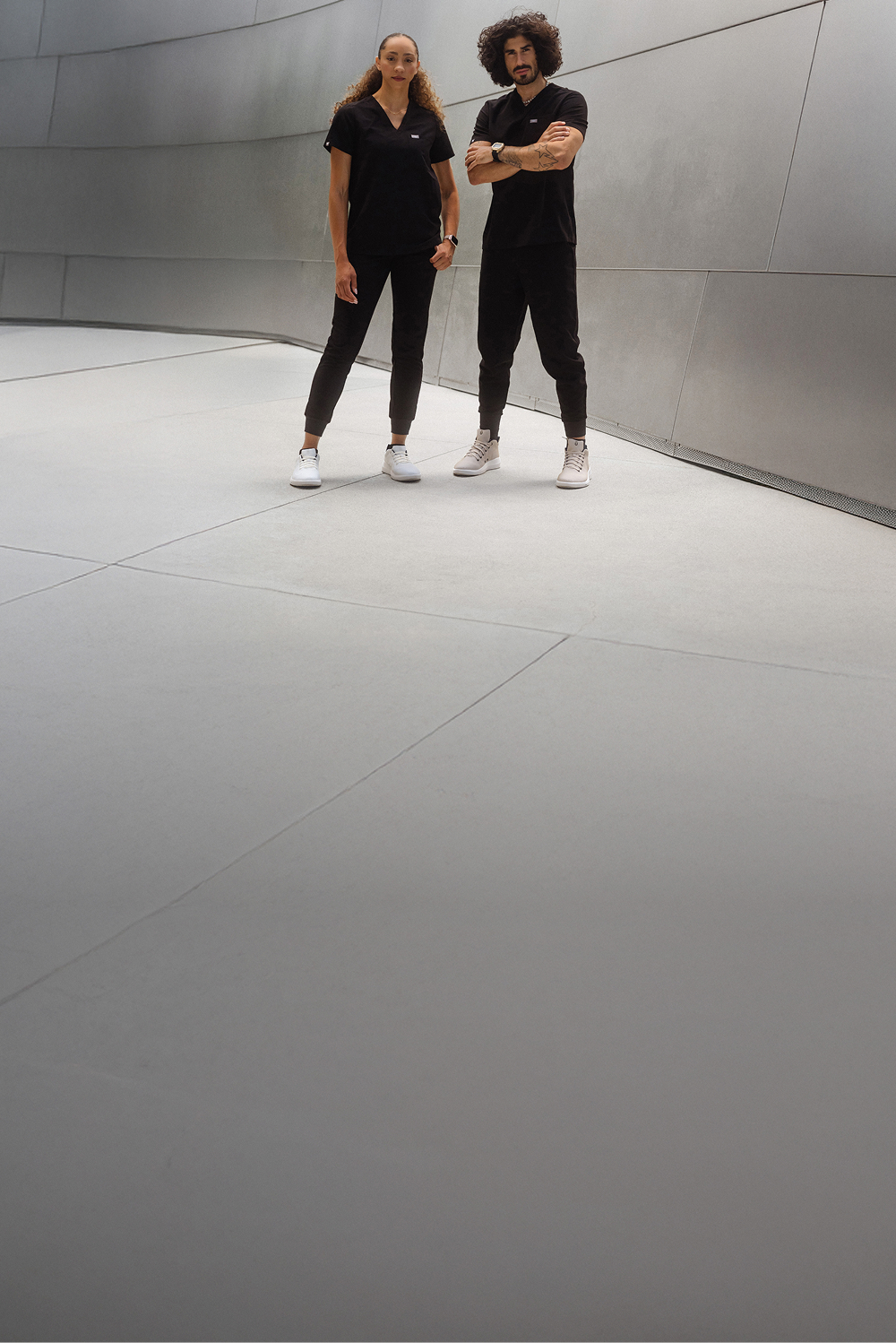 Two people in black outfits standing in a modern, minimalist space.