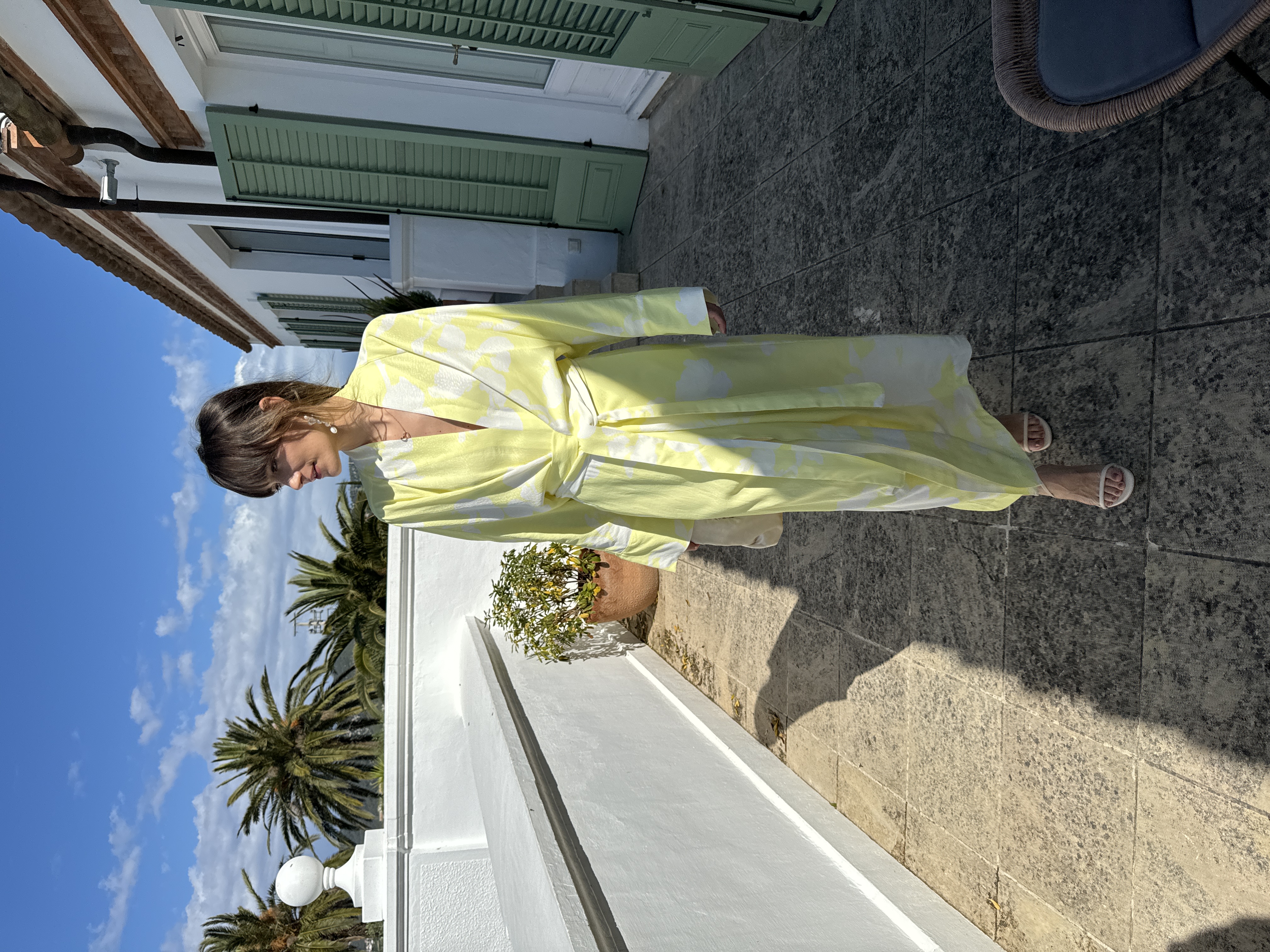 Person in a floral robe standing in sunlight near stairs.
