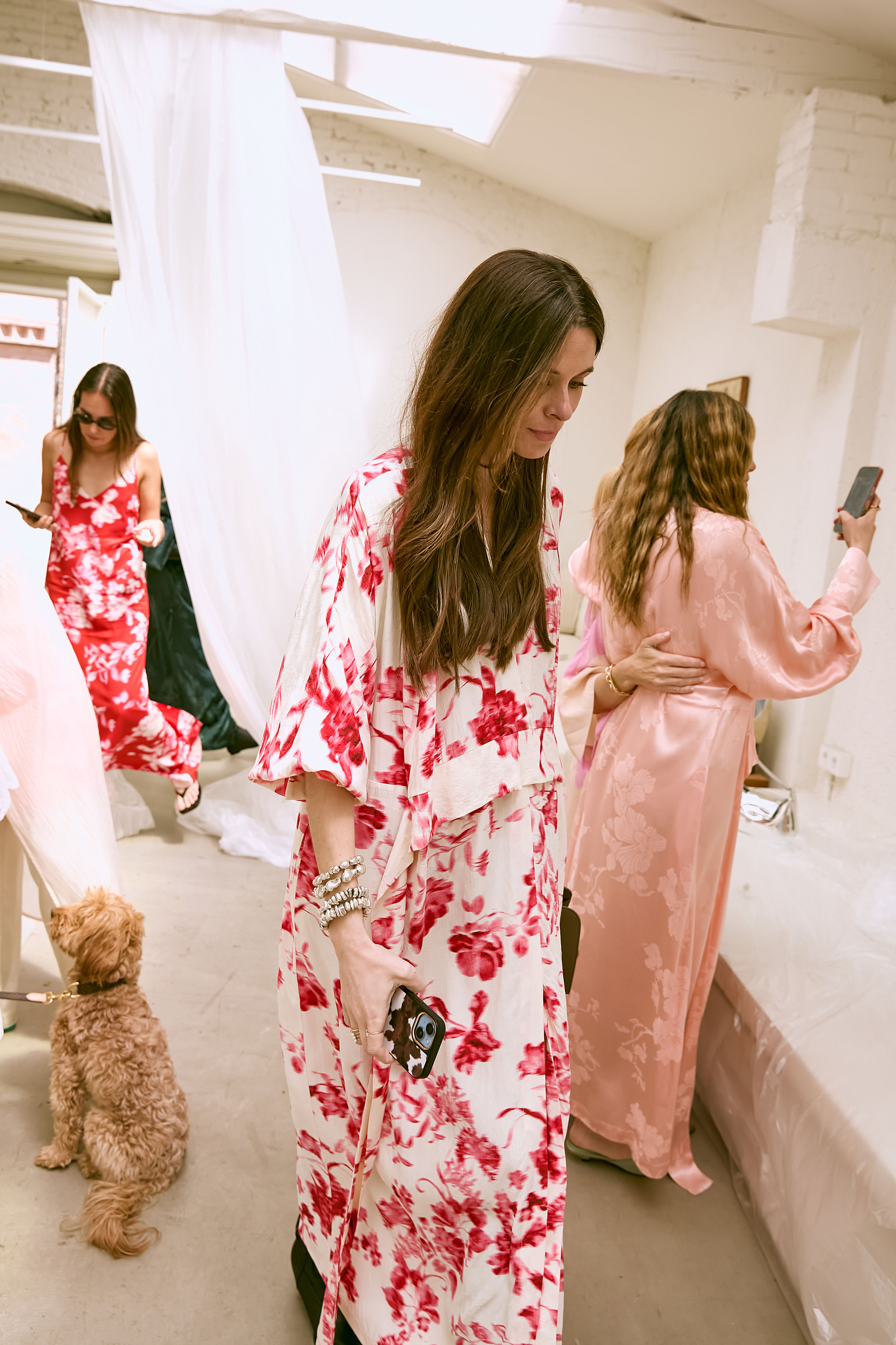 Women in floral dresses with a small dog indoors.