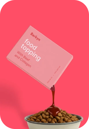 A pink packet of Barkyn food topping being poured over a bowl of dog kibble.