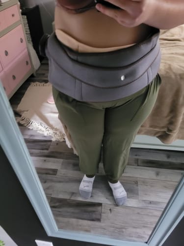 Person wearing a waist support belt, green pants, and socks, standing in front of a mirror.