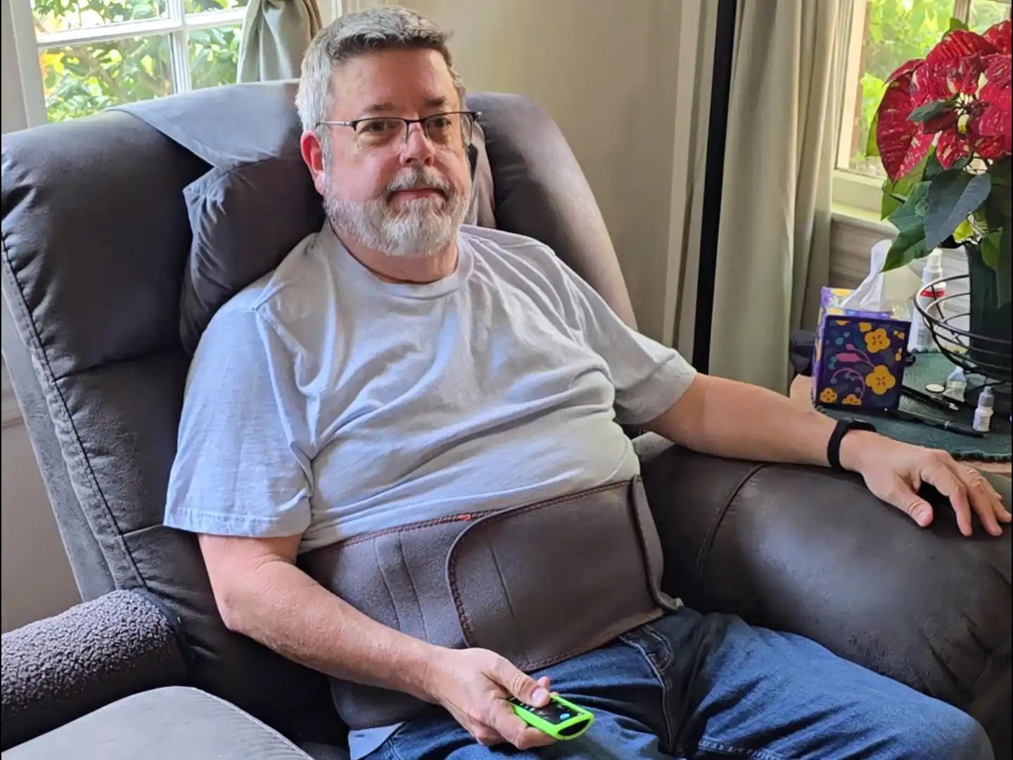 Man sitting in a recliner with a remote, wearing a back brace.