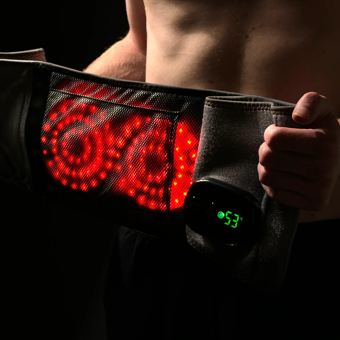 Person holding a heated belt with glowing red lights and digital temperature display.