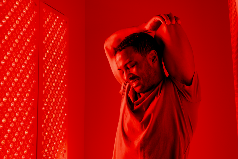 Person stretching in red-lit room with LED panel.