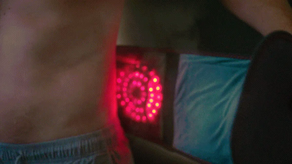Person using a red light therapy device on their back.