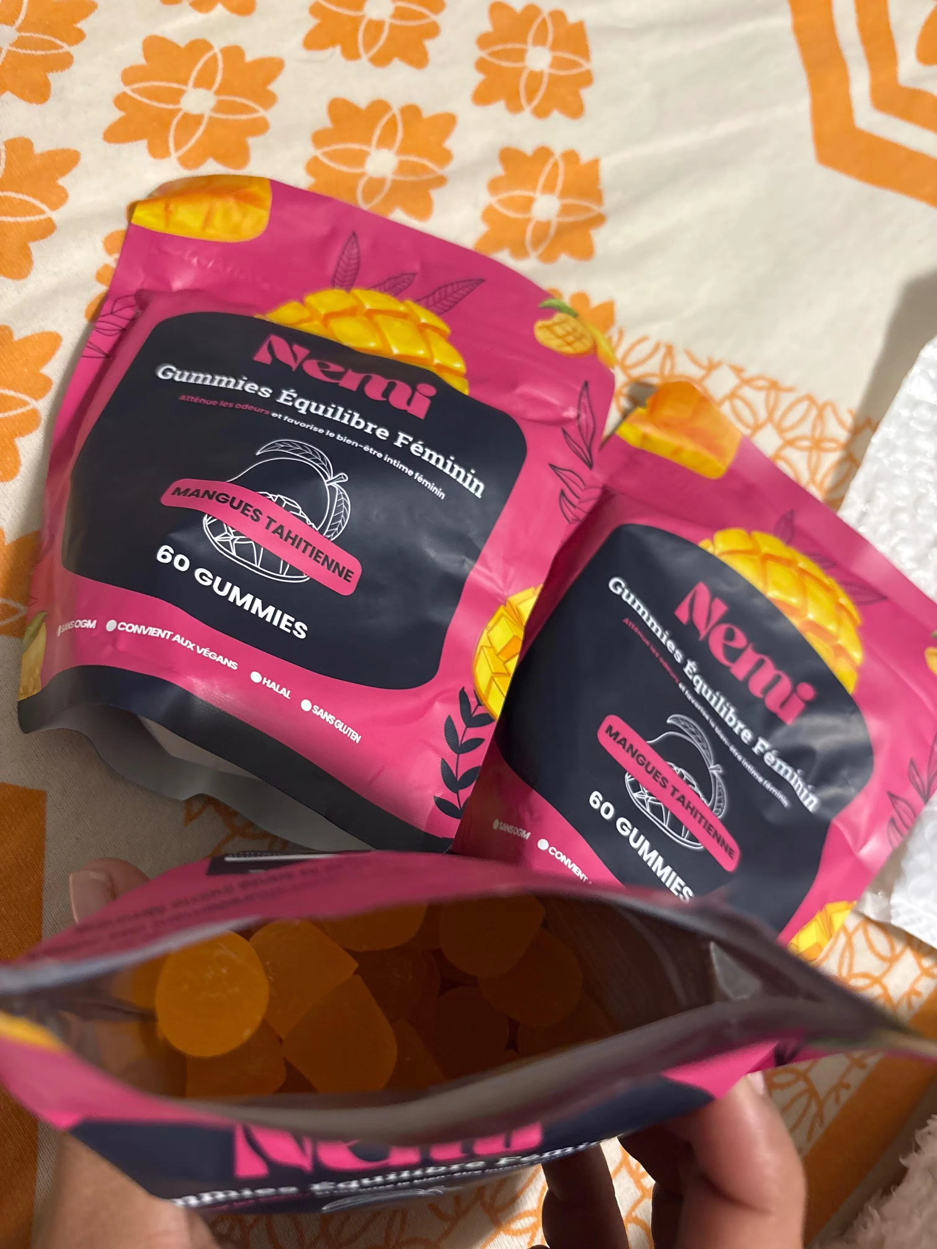 Three pink and black packages of gummies on a floral orange and white background.