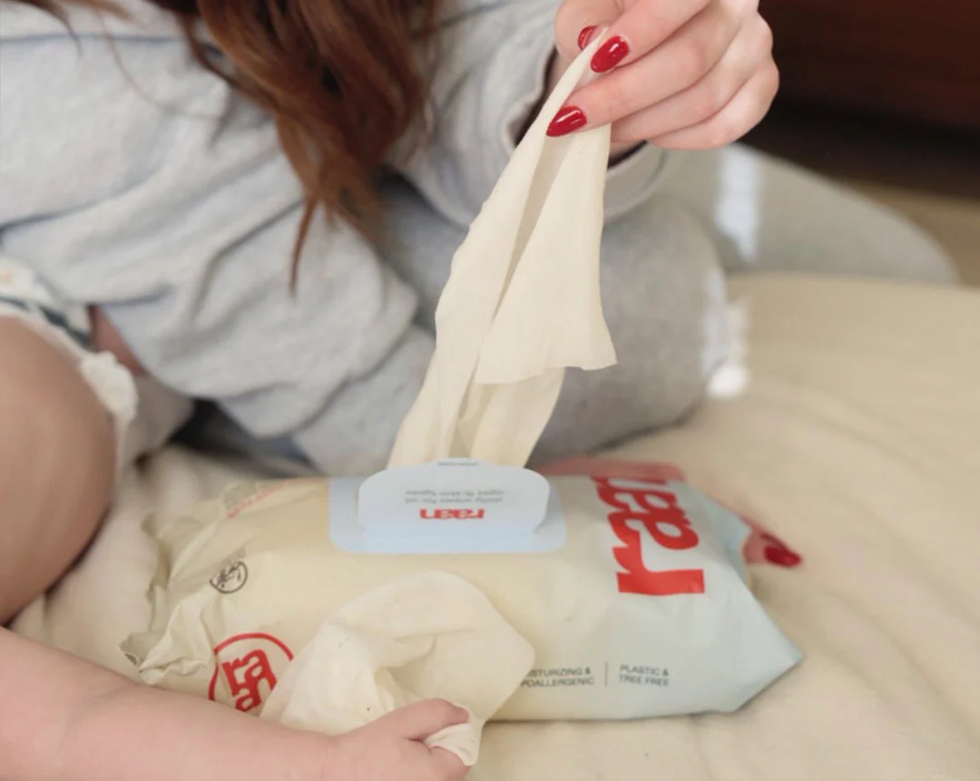 A person with red nail polish pulls a single wipe from a package of Raan brand wipes.