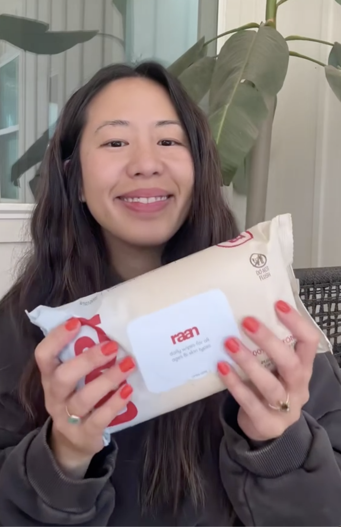 A smiling woman with red nail polish holds up a package of Raan daily wipes.