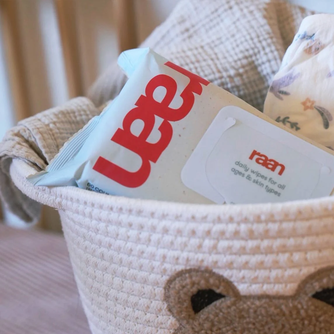 A package of raan daily wipes sits in a woven basket with a diaper and a blanket.
