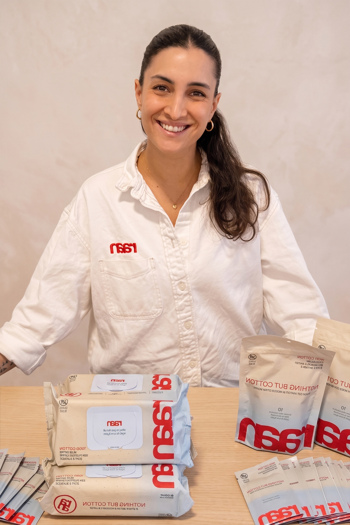 A smiling woman in a white shirt stands behind a table displaying branded products like wipes and packets.