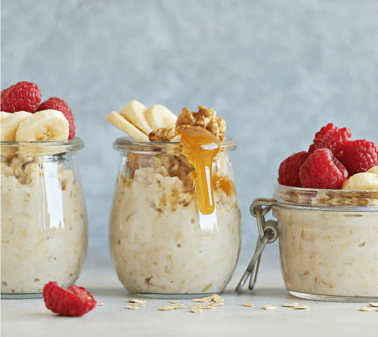 Three jars of oatmeal with bananas, raspberries, and honey.