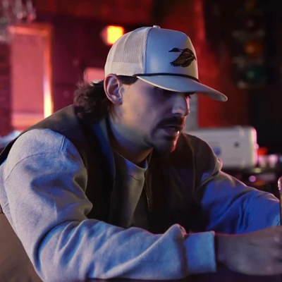 Man in a cap sitting at a bar with dim lighting.