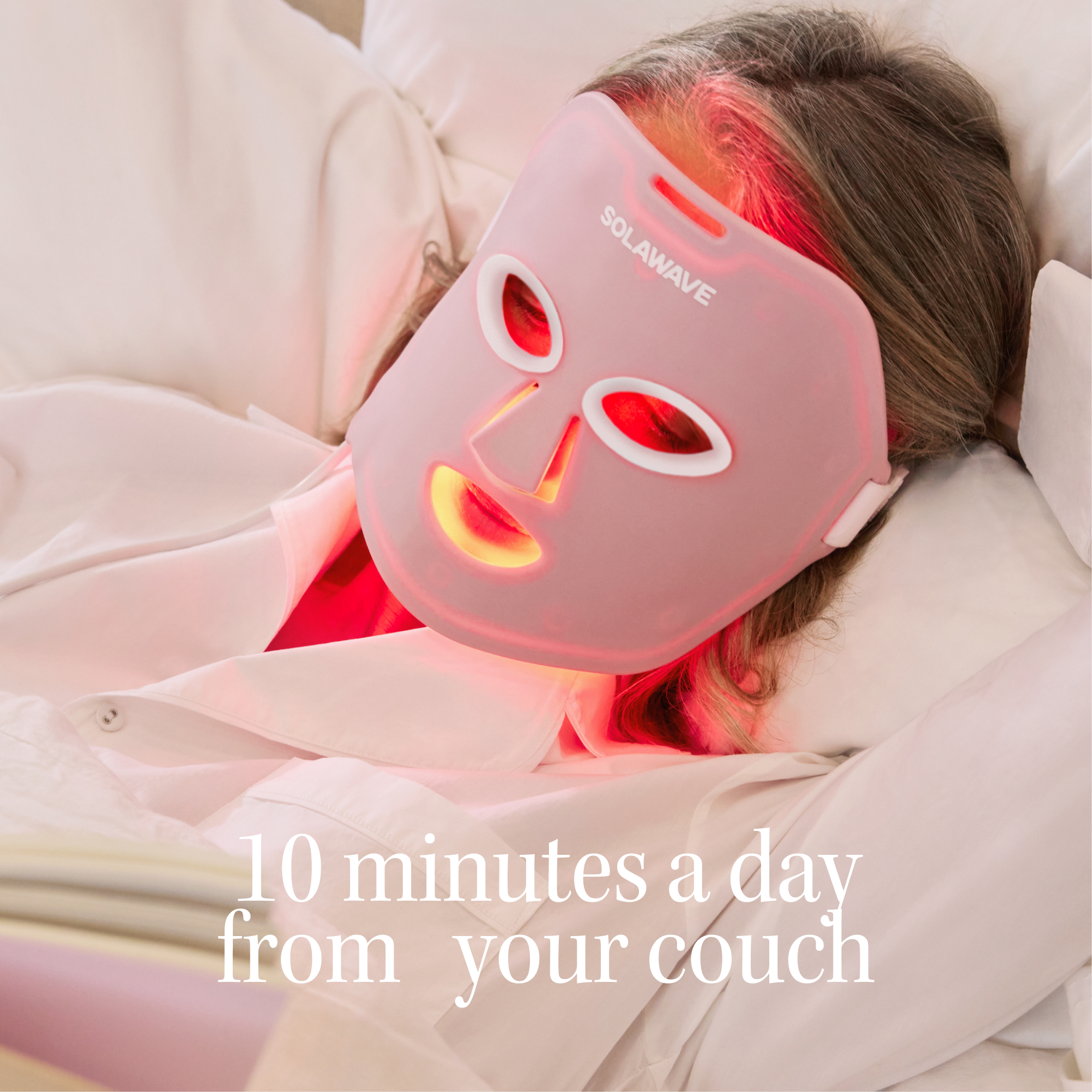 Person wearing a red light therapy mask, lying on a couch.