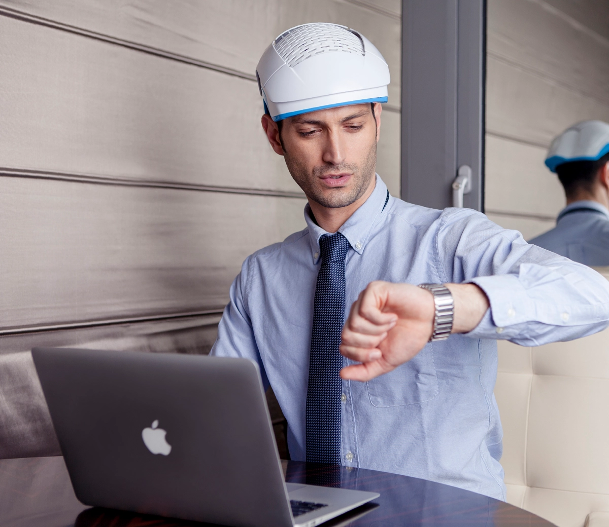 Man in a helmet looking at his watch while using a laptop.