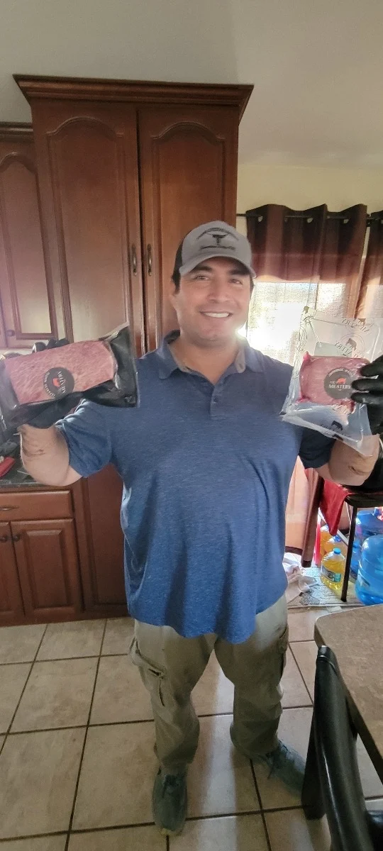 Person in a kitchen holding two packages of meat, smiling.