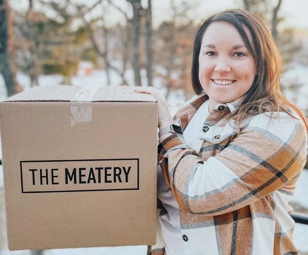 Person holding a large box labeled 'The Meatery' outdoors.