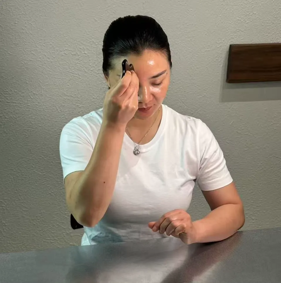 Person using a black tool on forehead, seated at a table.