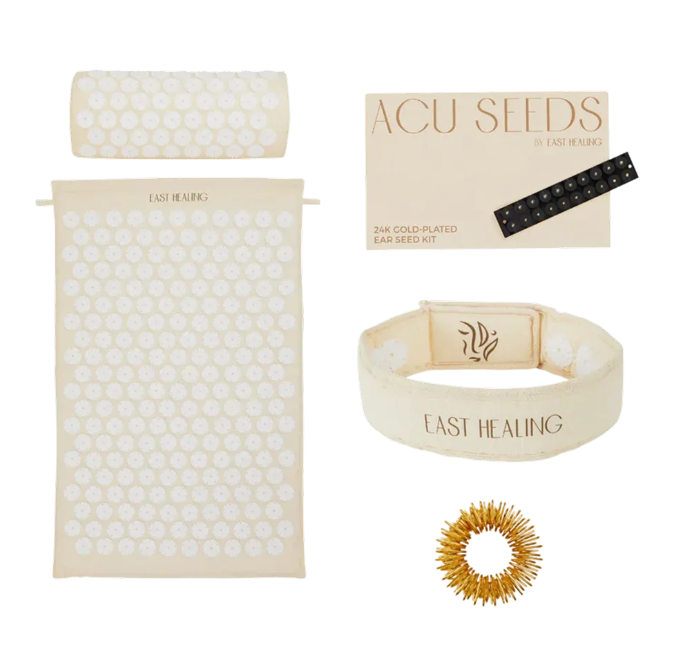 A collection of East Healing acupressure products including a mat, pillow, ear seeds, wristband, and massage ring.