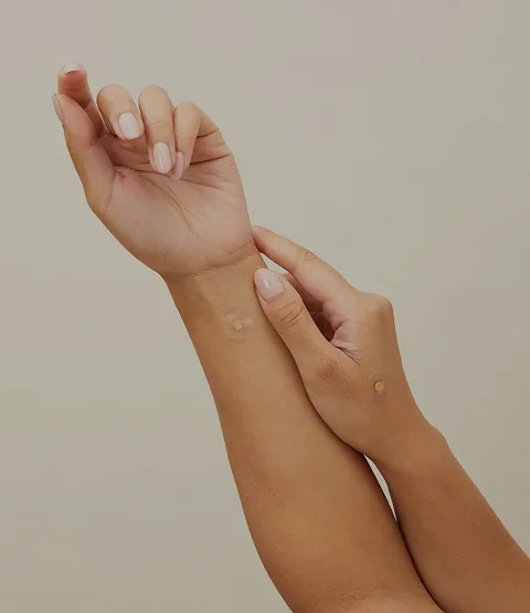 A person's arms and hands with two small, round, skin-colored patches applied to the skin.