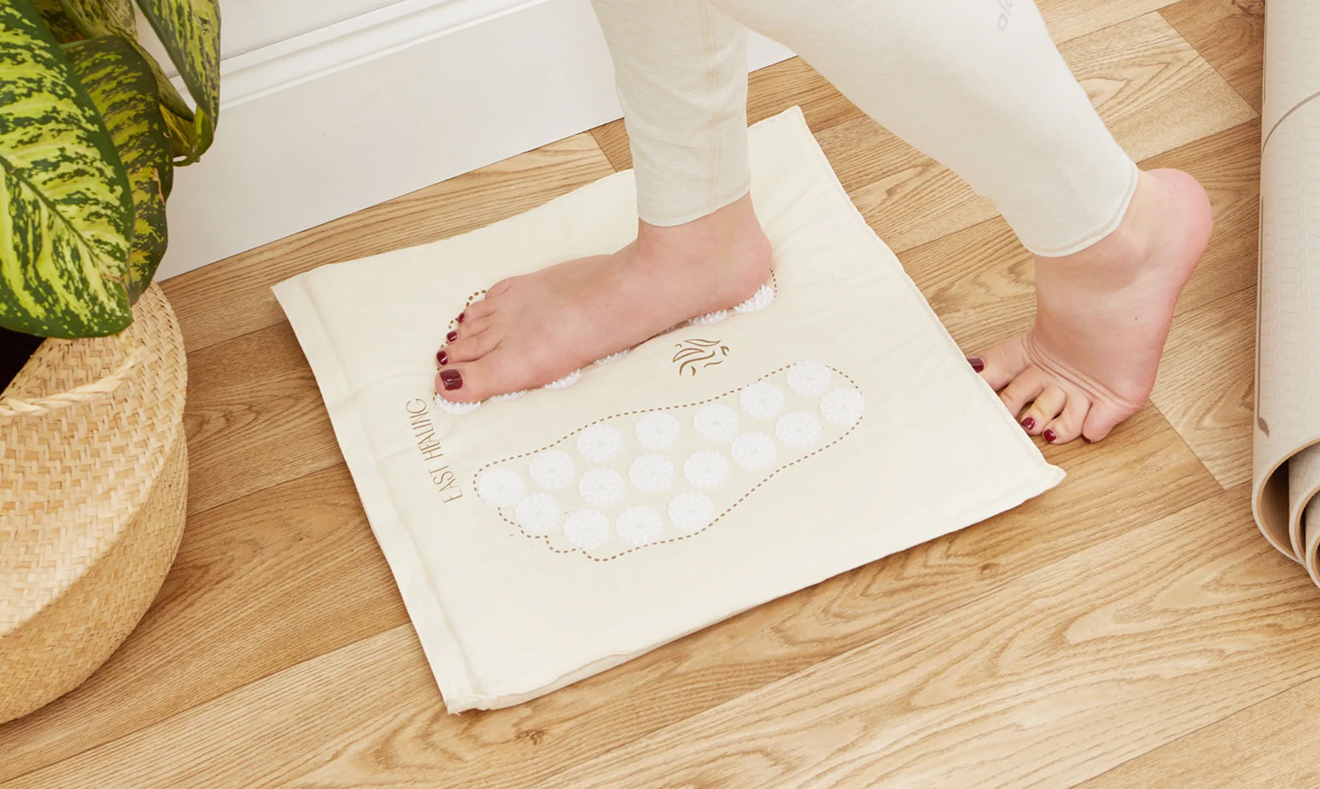 Foot on acupressure mat with plant and yoga mat nearby.