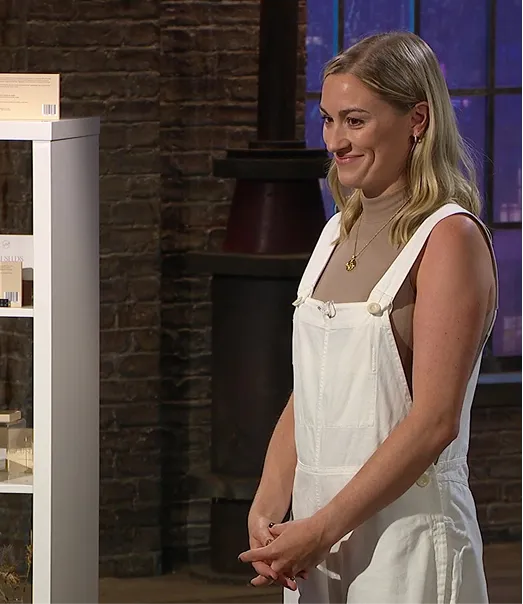 Woman in white overalls smiling next to a display shelf.