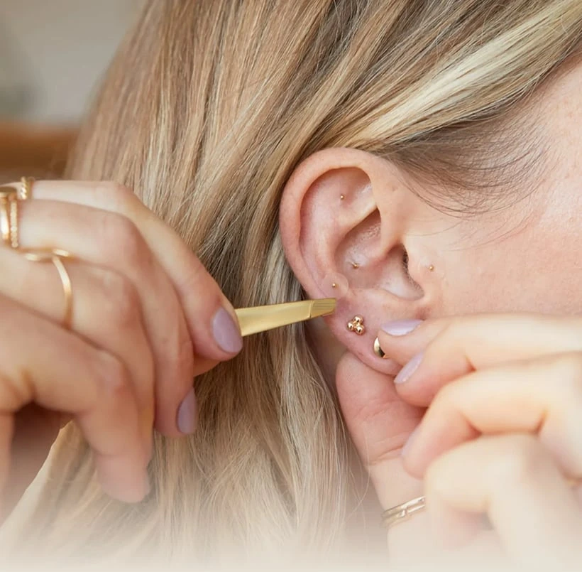 Person using tool near ear with earrings.