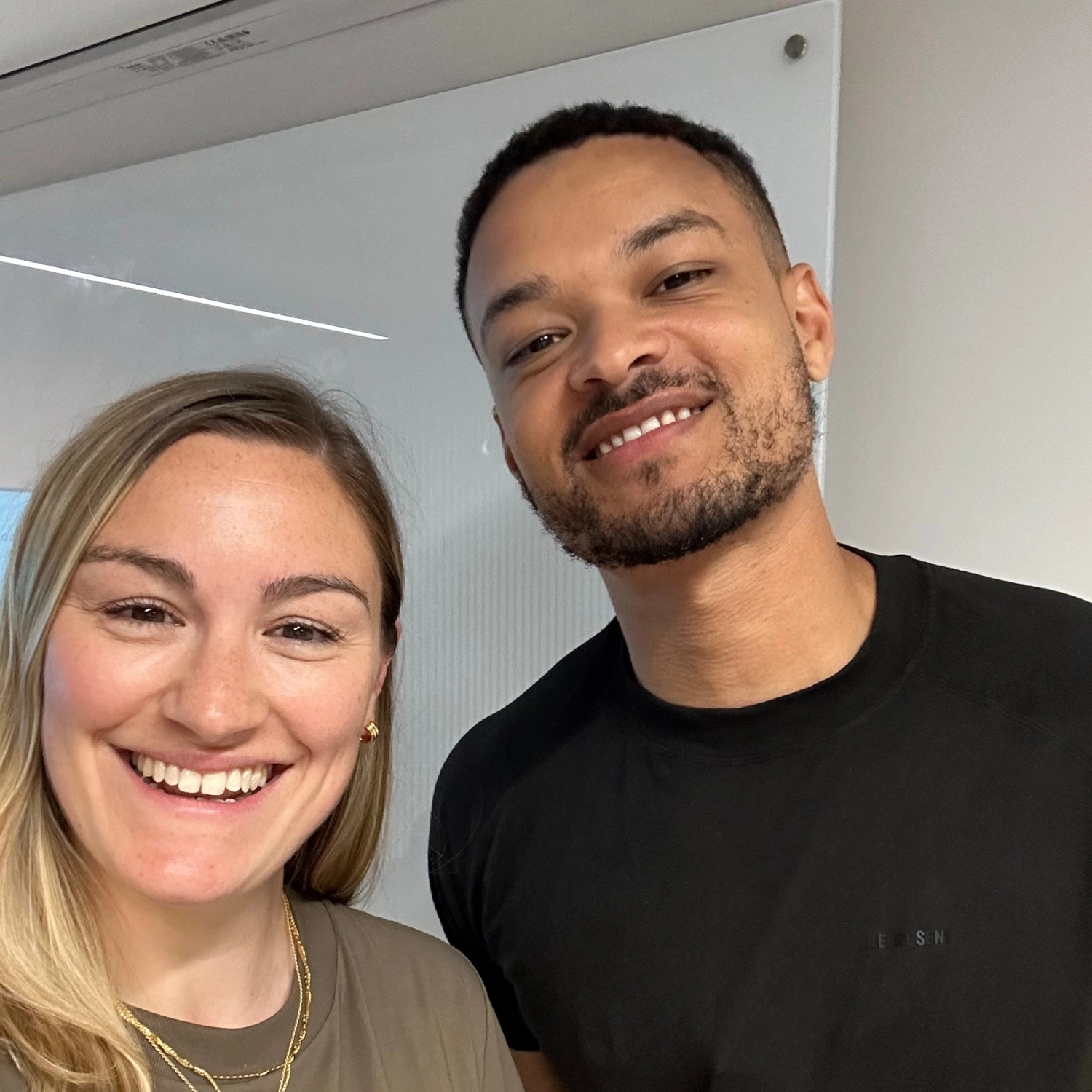 Two people smiling, standing close together indoors.