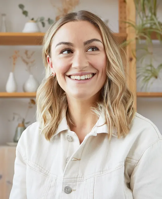 Person smiling in a room with shelves and plants.
