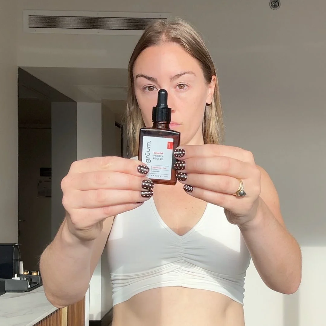 A woman with polka dot nails holds a small bottle of Grüum Botanisk Prickly Pear Oil.