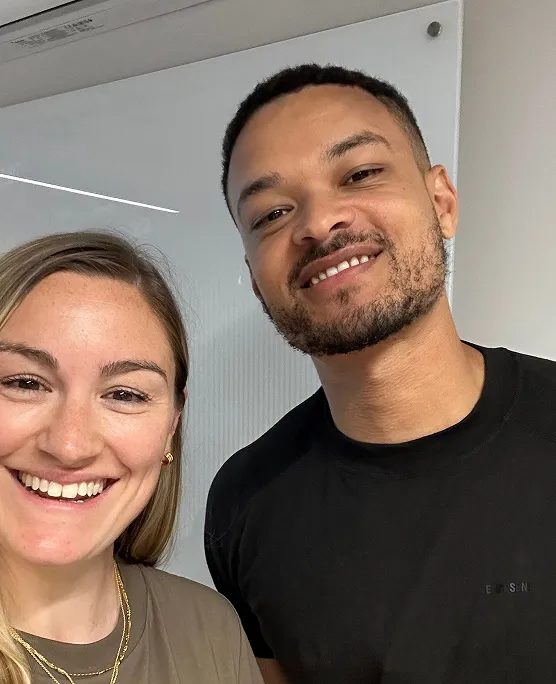 A close-up selfie of a smiling woman and a smiling man standing next to each other indoors.