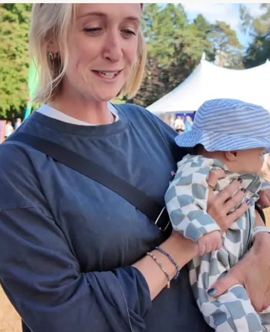 Person holding a baby wearing a striped hat outdoors.