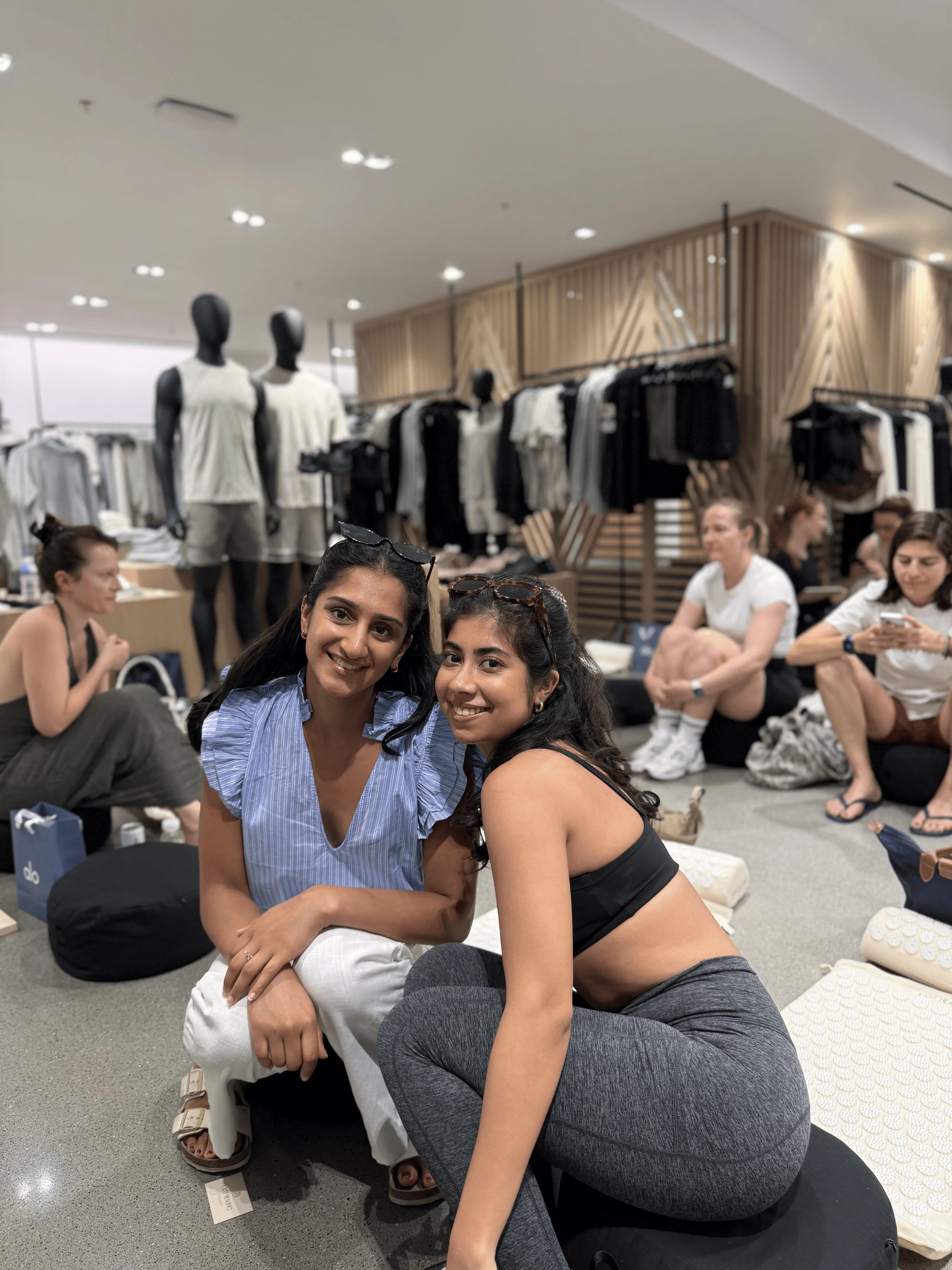 People sitting on the floor in a clothing store, mannequins in the background.