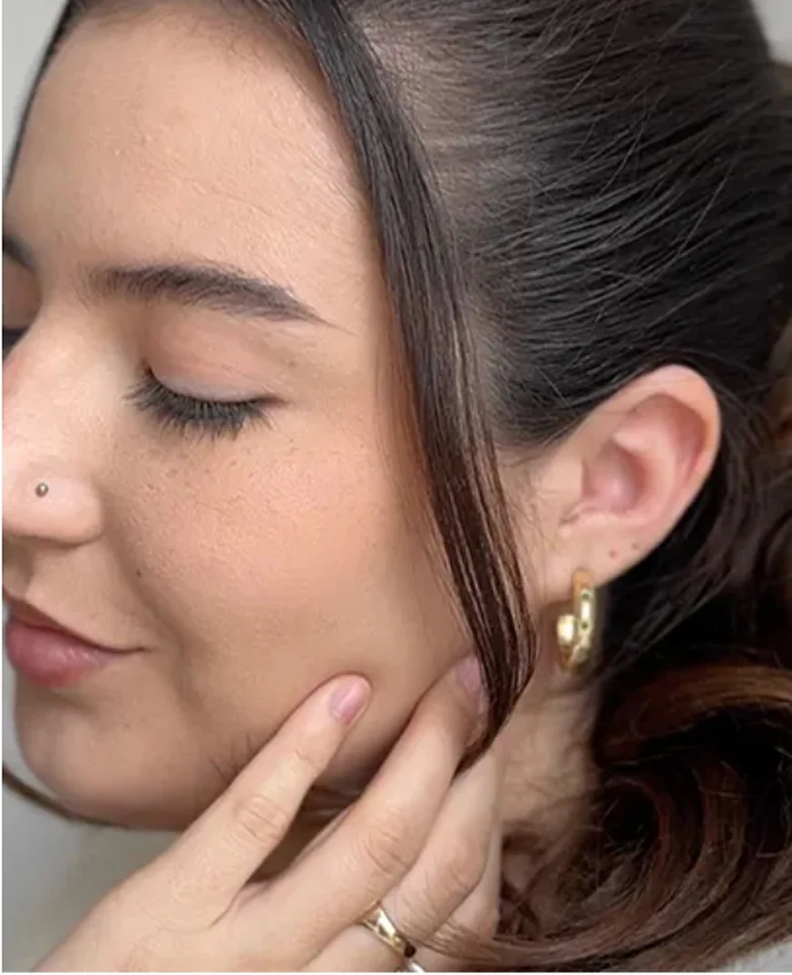 A close-up of a woman with her eyes closed, touching her cheek, wearing a gold hoop earring.
