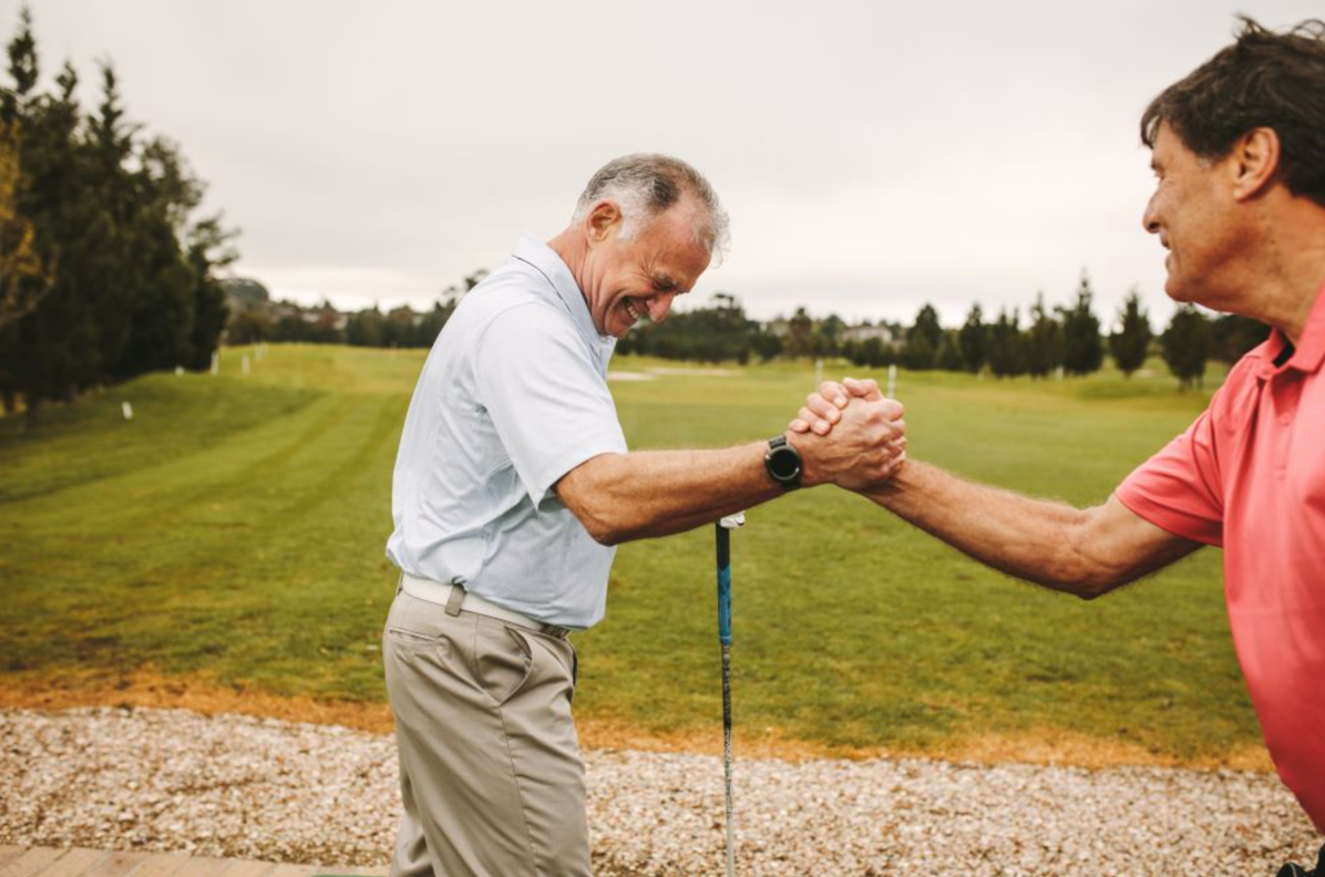 Two men shaking hands on a golf course, smiling.