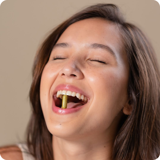 Smiling woman holding a green capsule between her teeth.