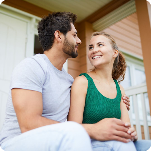 A couple sitting and smiling at each other on a porch.