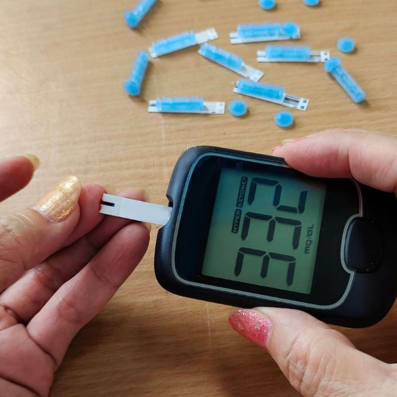 Person using a glucose meter with test strips on a wooden surface.