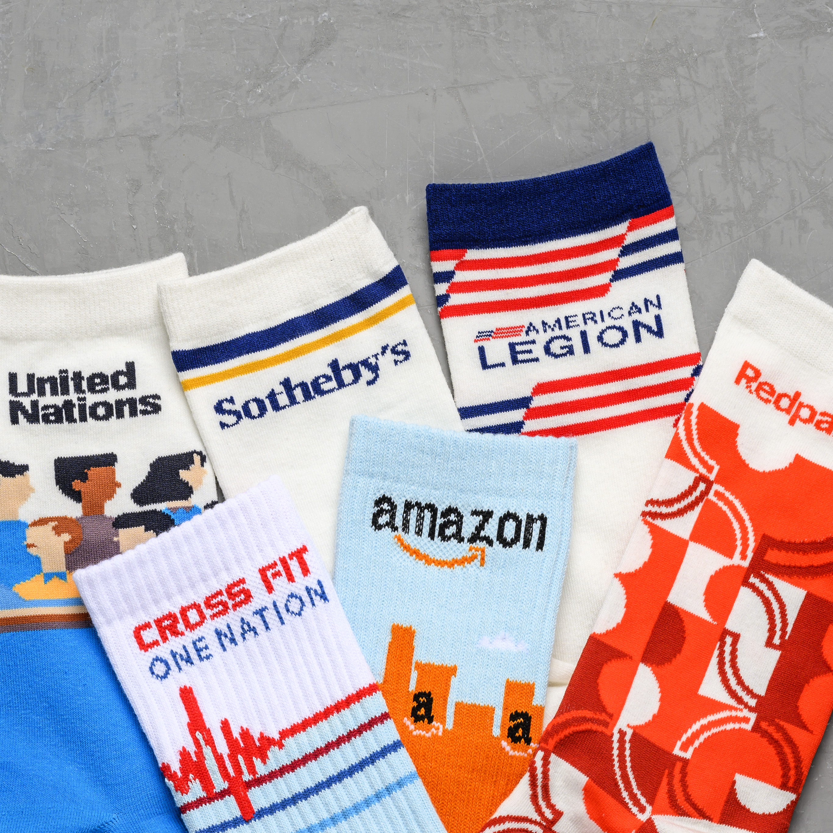 A collection of colorful socks with various brand logos laid out on a gray textured background.