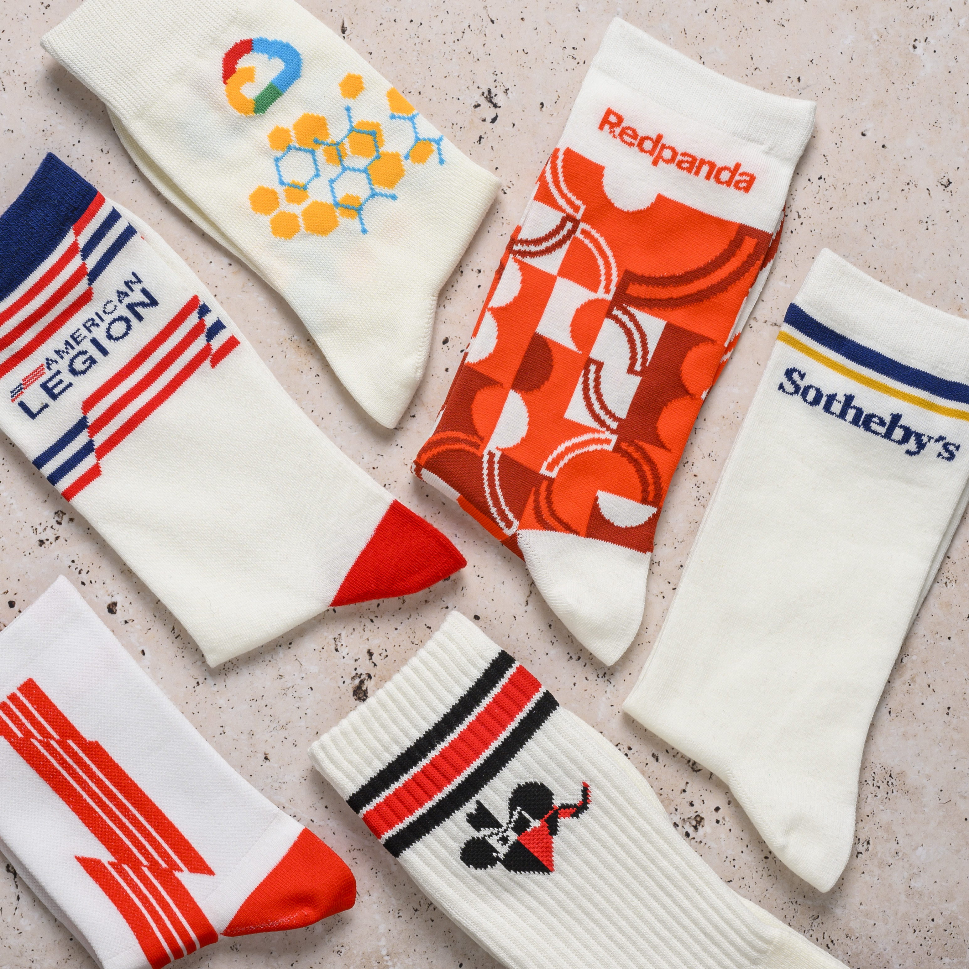 An overhead view of several pairs of white, custom-branded socks with colorful logos and patterns.