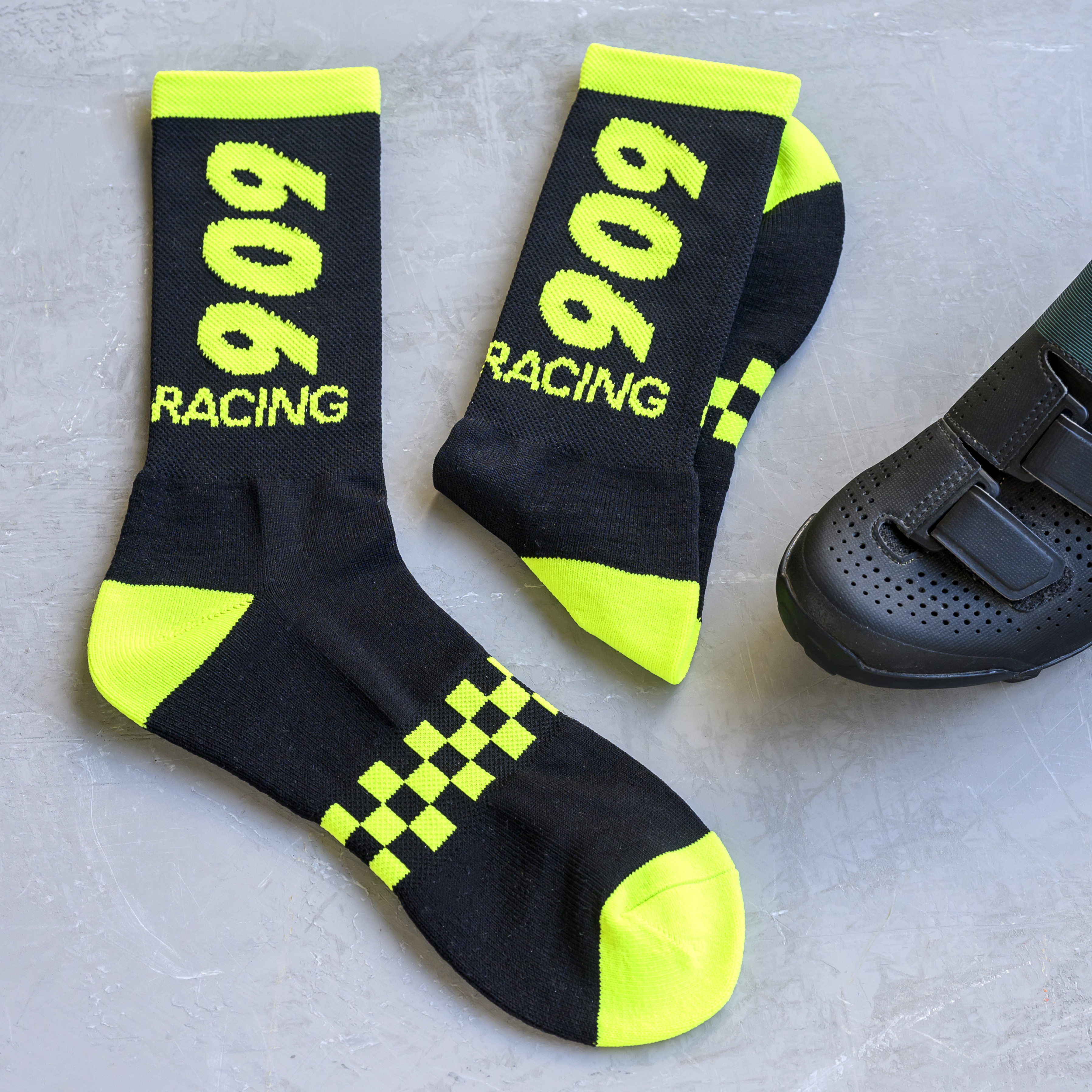 A pair of black and neon yellow '909 RACING' socks next to a black cycling shoe.
