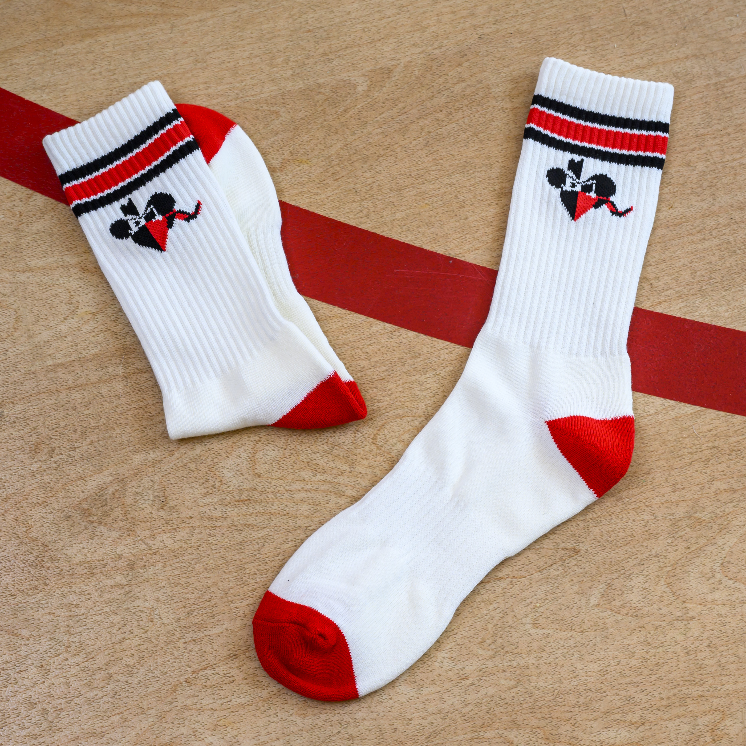 A pair of white socks with red heels and toes, striped cuffs, and a logo on a wood surface.