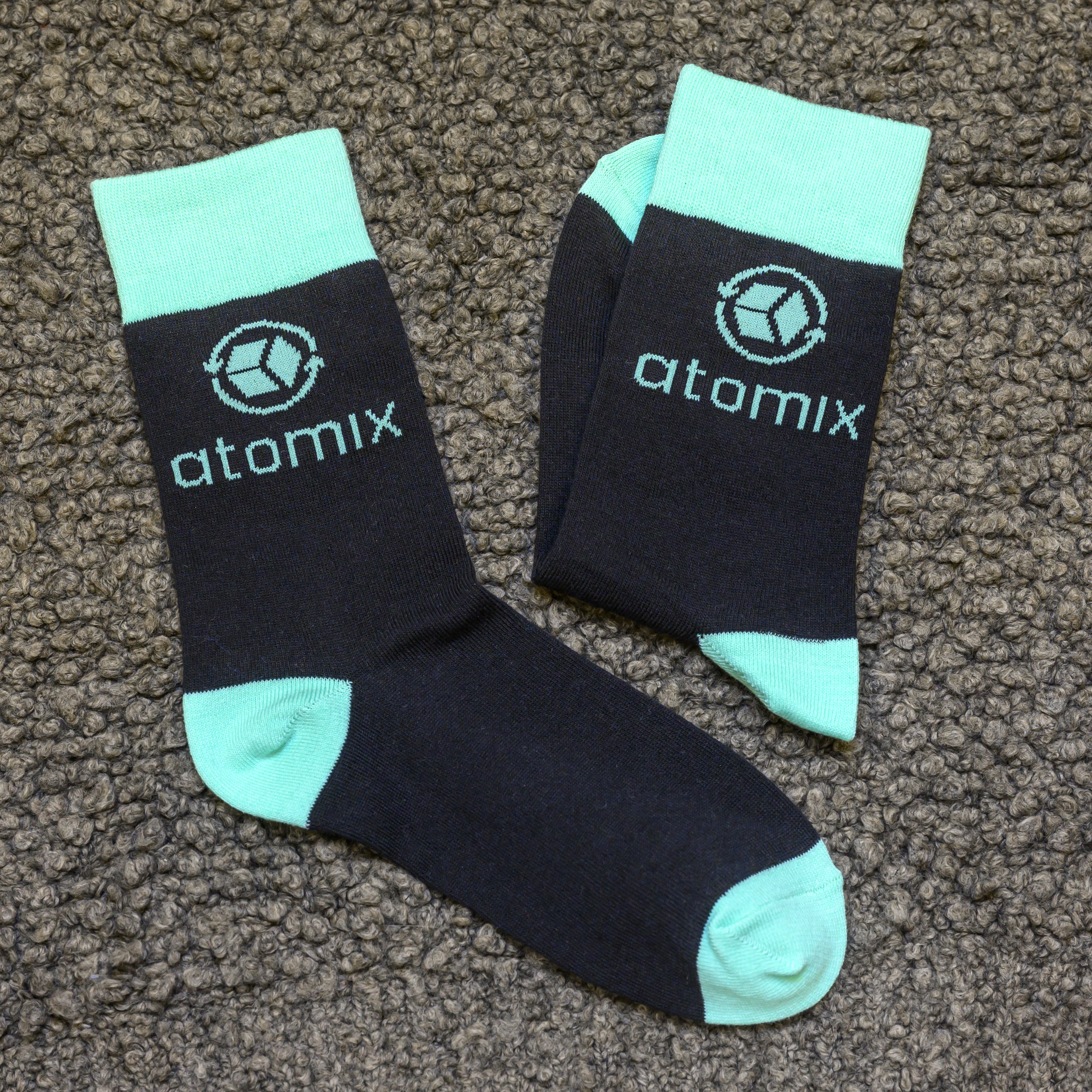 A pair of black and turquoise socks with the 'atomix' logo on them, lying on a shaggy rug.