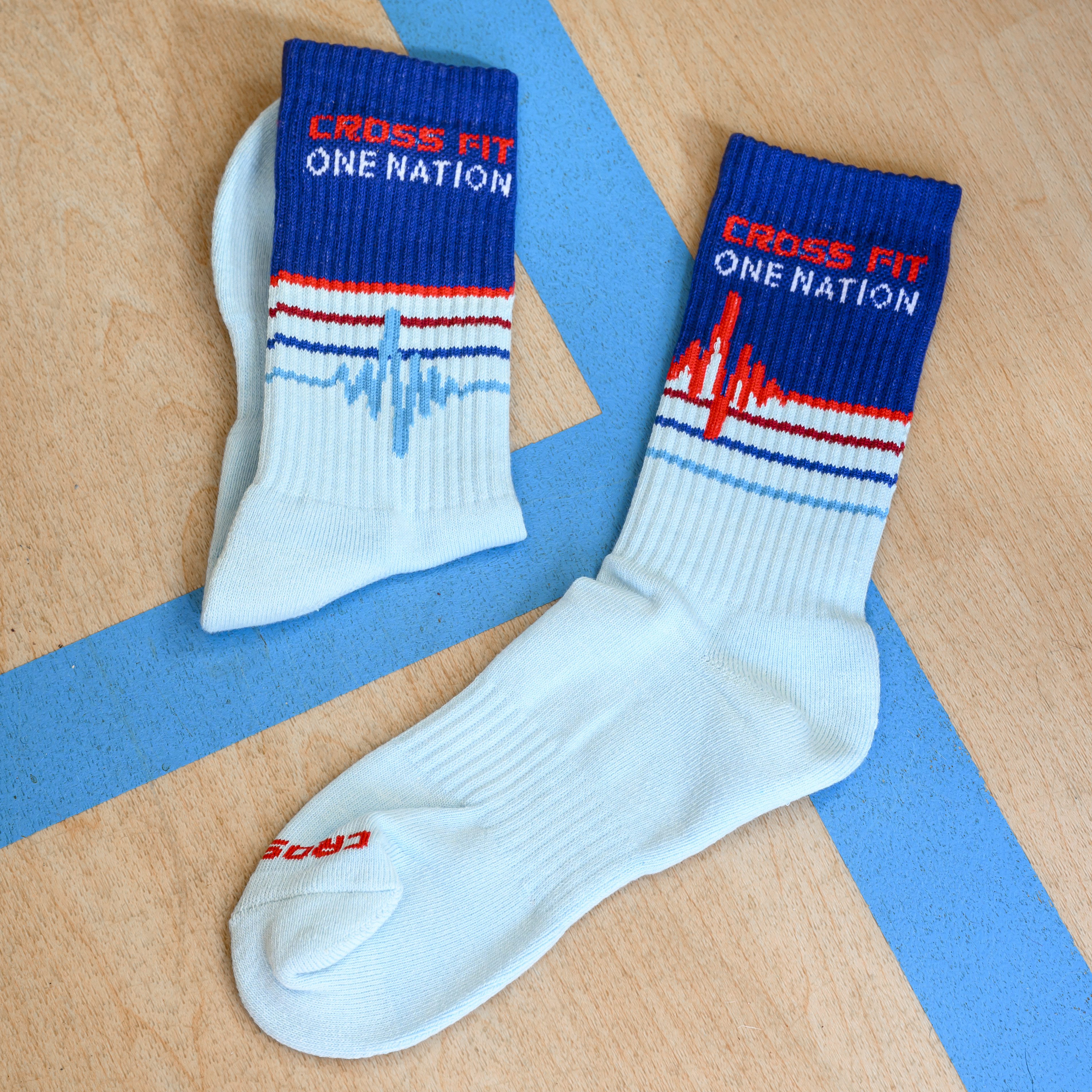 A pair of light blue and dark blue Cross Fit One Nation socks on a wooden surface.