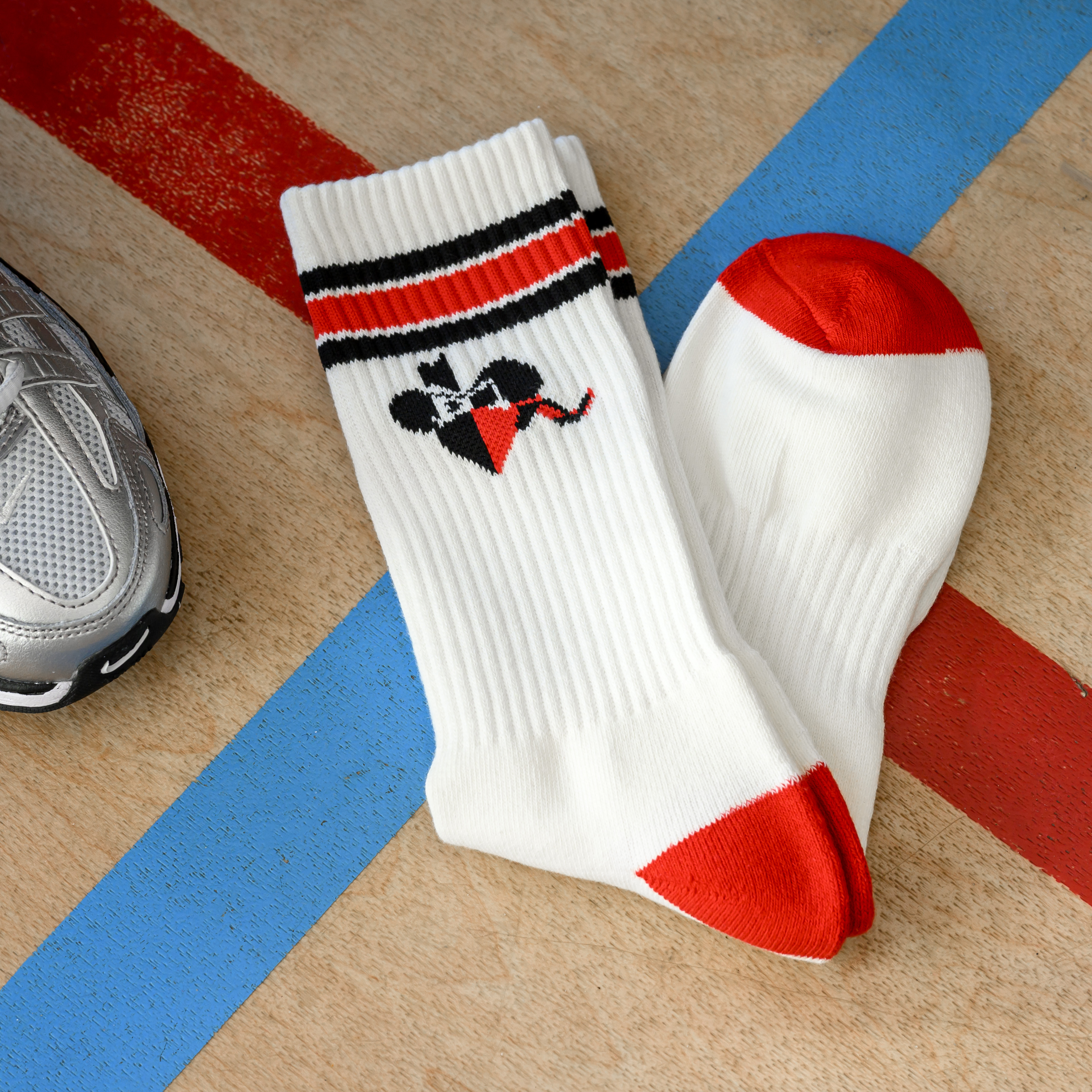 A pair of white socks with red heels and toes, striped cuffs, and a logo on a wood surface.
