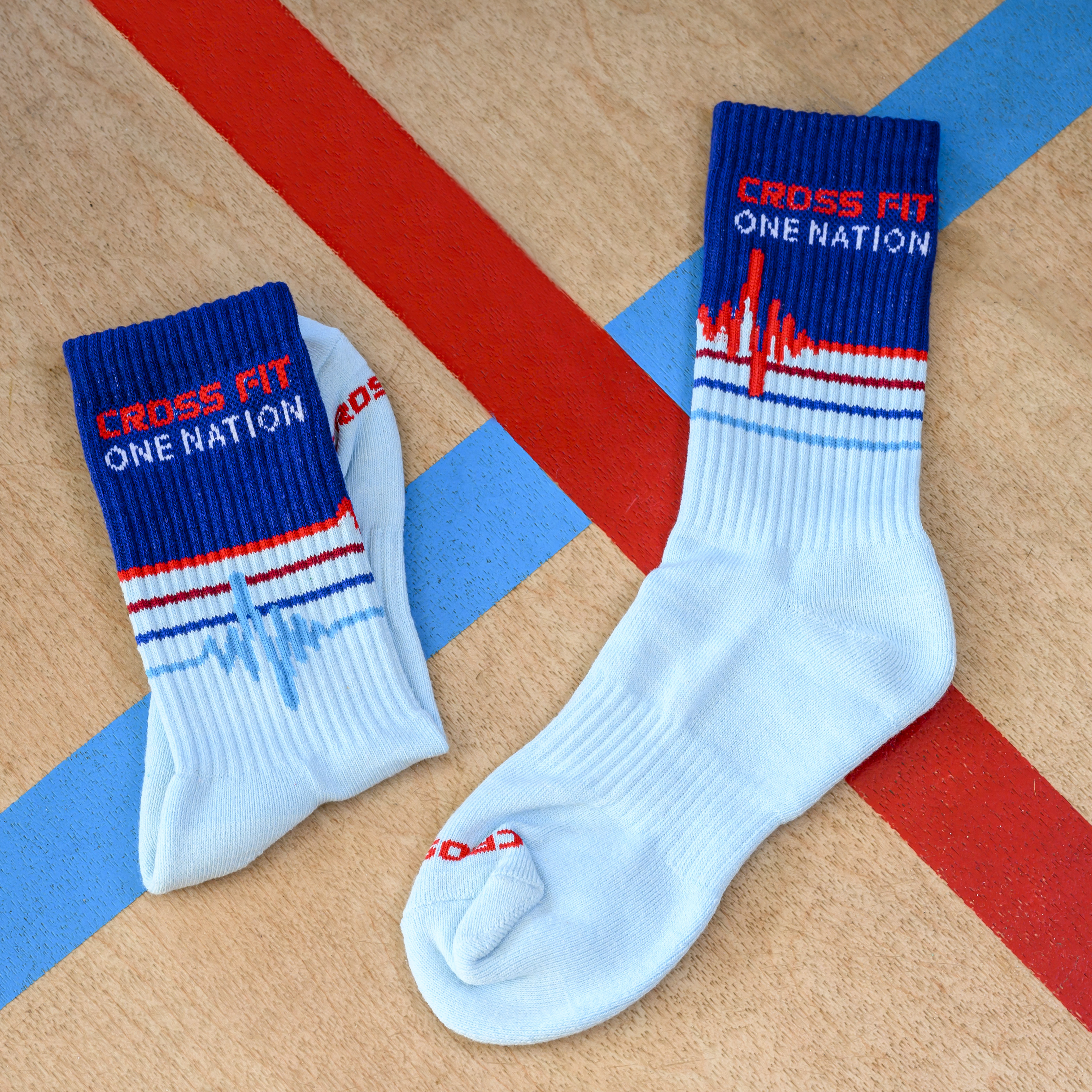 A pair of light blue socks with 'Cross Fit One Nation' on the cuff, on a striped surface.