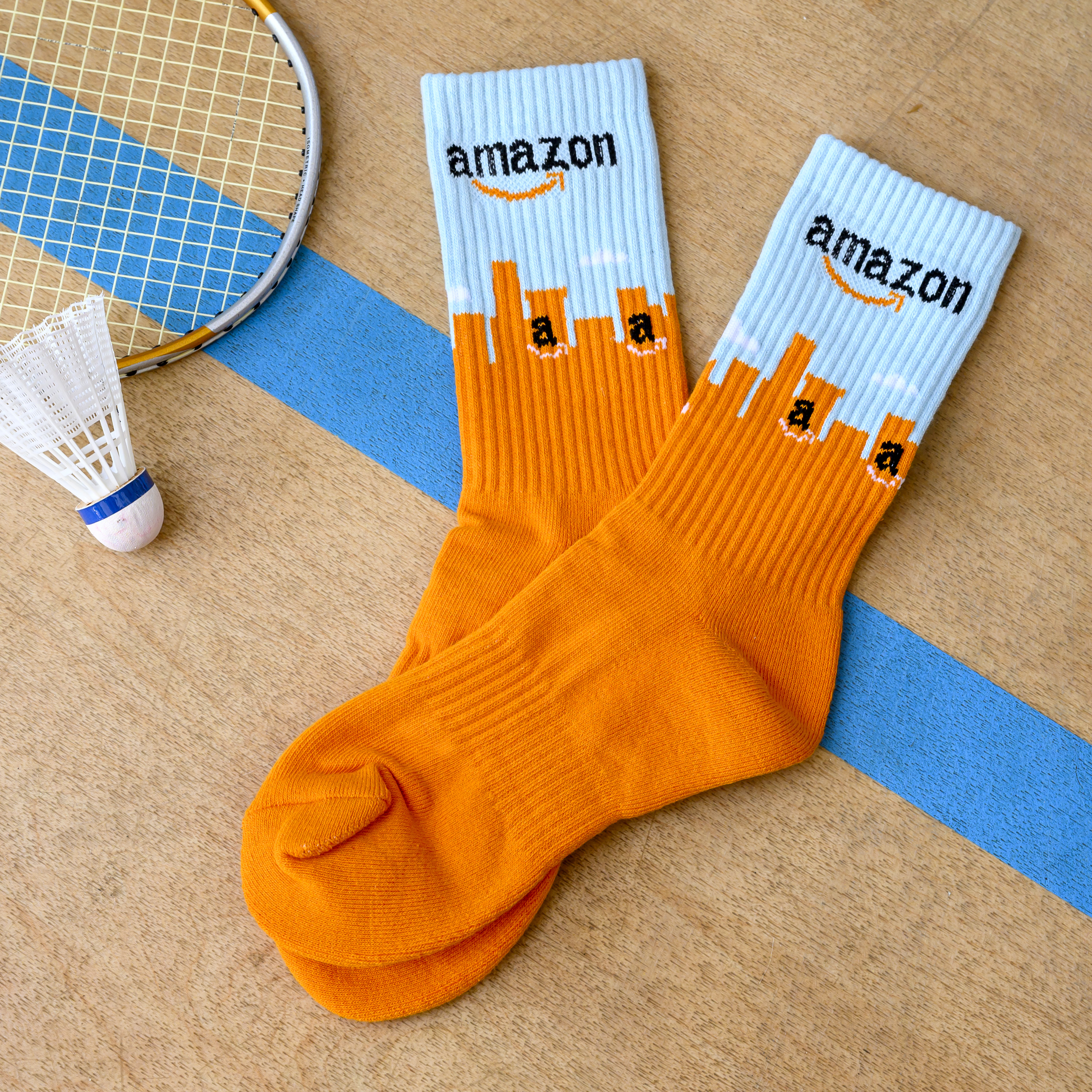 A pair of Amazon-branded socks lie on a badminton court next to a racket and shuttlecock.